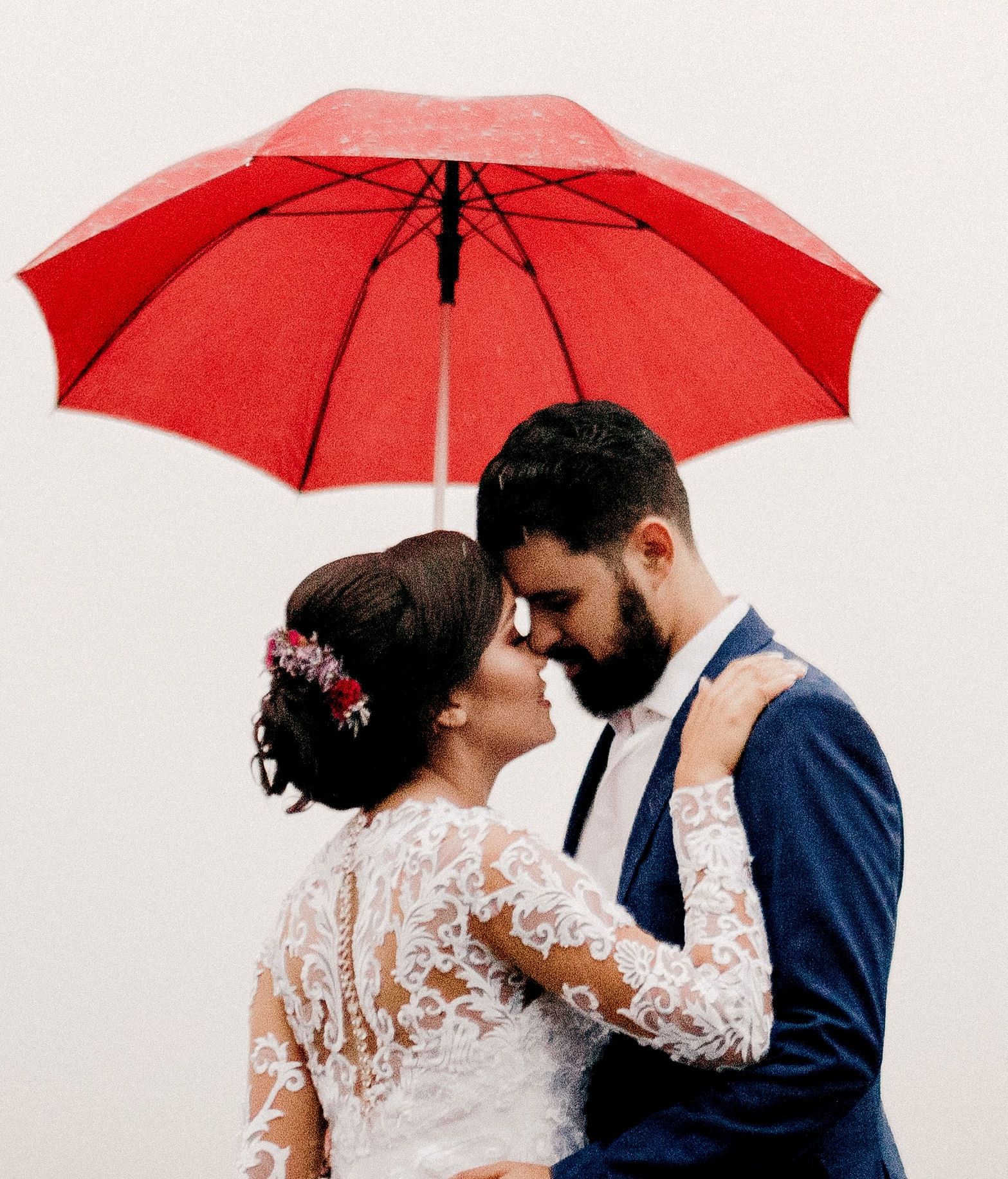 Bride and Groom embracing under a red
                        umbrella