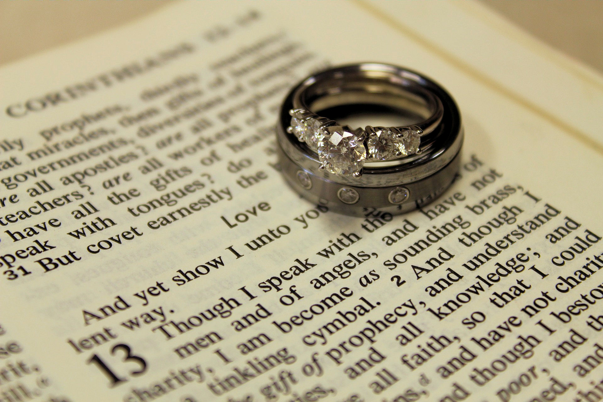 Bible open at 1
                    Corinthians 13 with wedding and engagement rings
                    lying on the page