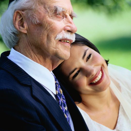 Bride resting her head
                      on her grandfather's shoulder. Both are smiling.