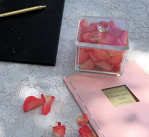 Naming Ceremony Table. White cloth, pink rose
petals, keepsake copy of the ceremony with pink
cover