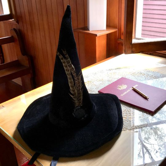 Signing
                      table next to an open window. On the table is the
                      marriage register, a gold pen, and Professor
                      McGonagall's hat