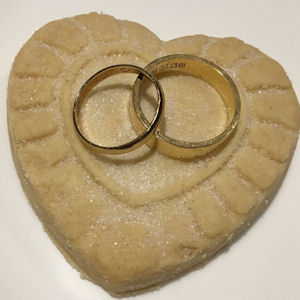 Two gold wedding rings on a heart-shaped
                    shortbread biscuit