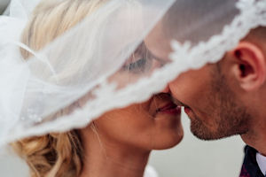 White bride and groom kissing under bridal
                    veil