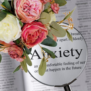 Bouquet of white and various shades of pink
                    peonies with gum leaves on a page with a magnifying
                    glass enlarging the word Anxiety