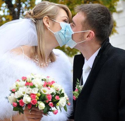 Bride and Groom kissing wearing surgical
                        masks