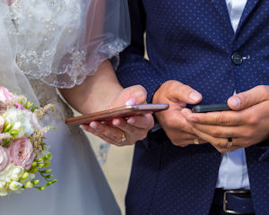 Bride and Groom texting on their phones.
                          Bride holds a pastel bouquet. Groom wears a
                          cobalt blue suit.