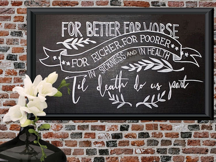 Chalkboard with the
                      traditional wedding vows hanging on a brick wall
                      with a black vase of white flowers in front of it