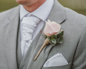 Man wearing a grey
                        suit with a pink rose pinned to the lapel and a
                        white pocket square in the breast pocket