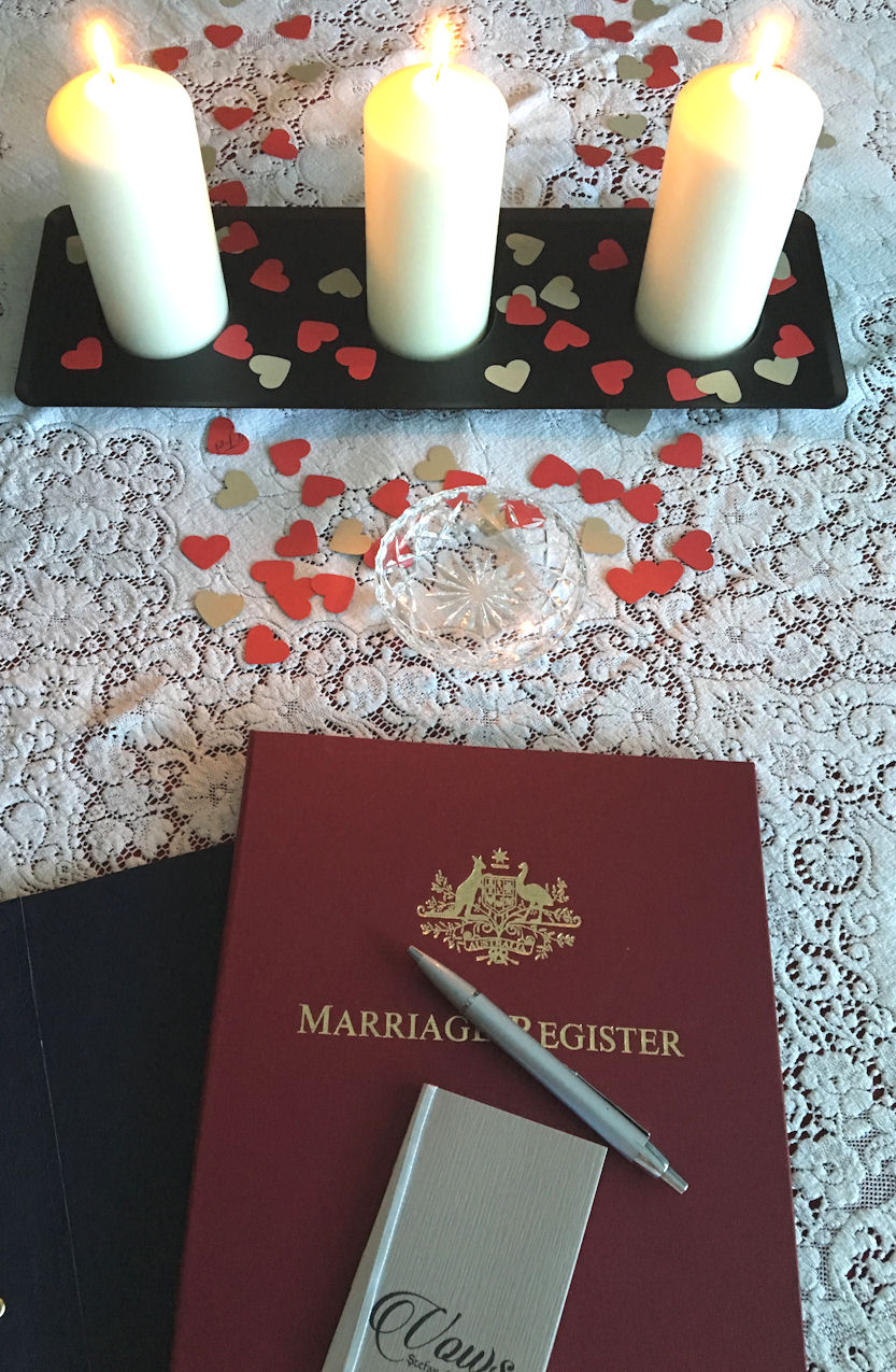 Marriage Register on table with three candles,
                    heart confetti, glass ring dish, lace tablecloth