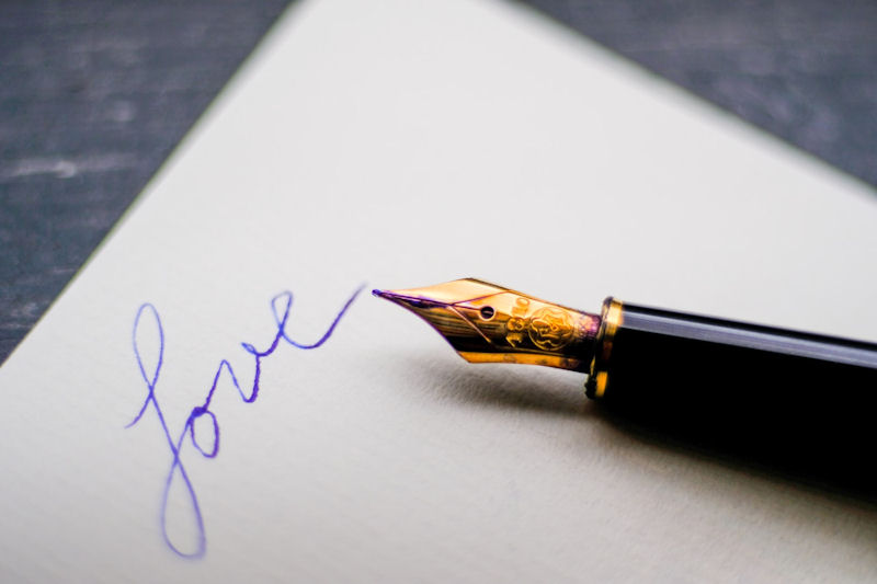 Black fountain pen lying on a sheet of
                        white paper on which the word Love has been
                        written in blue ink