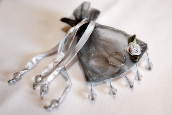 Wedding rings in a silver organza ring
                        bag trimmed with beads and silk roses