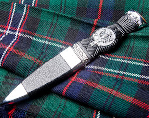 A Scottish sgian dubh, sheathed, lying on
                          a tartan kilt