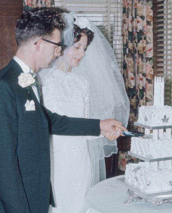 Vintage photograph of couple cutting a three
                      tier wedding cake