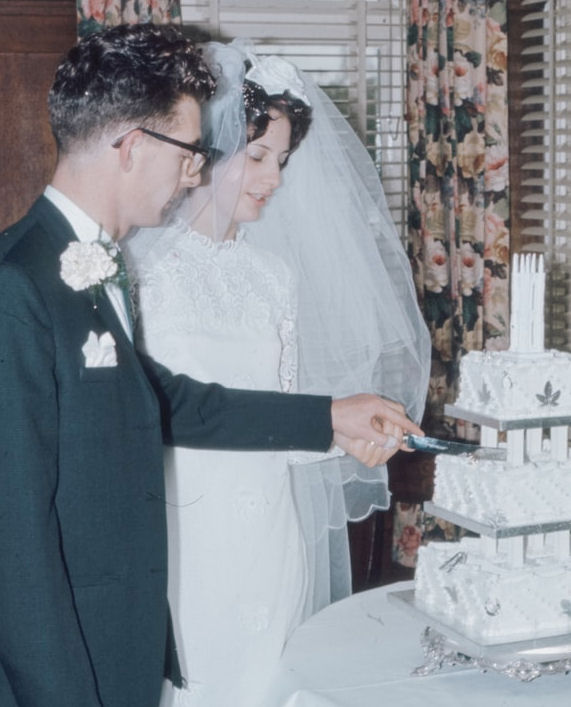 Vintage photograph of couple cutting a three
                      tier wedding cake