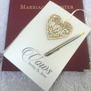 Vows booklet on a Marriage Register with a
                    silver and gold pen and a filigree wooden heart