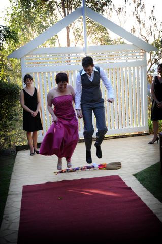 Paula and Michelle jumping the broom after
                        their commitment ceremony conducted by Jennifer
                        Cram, Pride Ceremonies